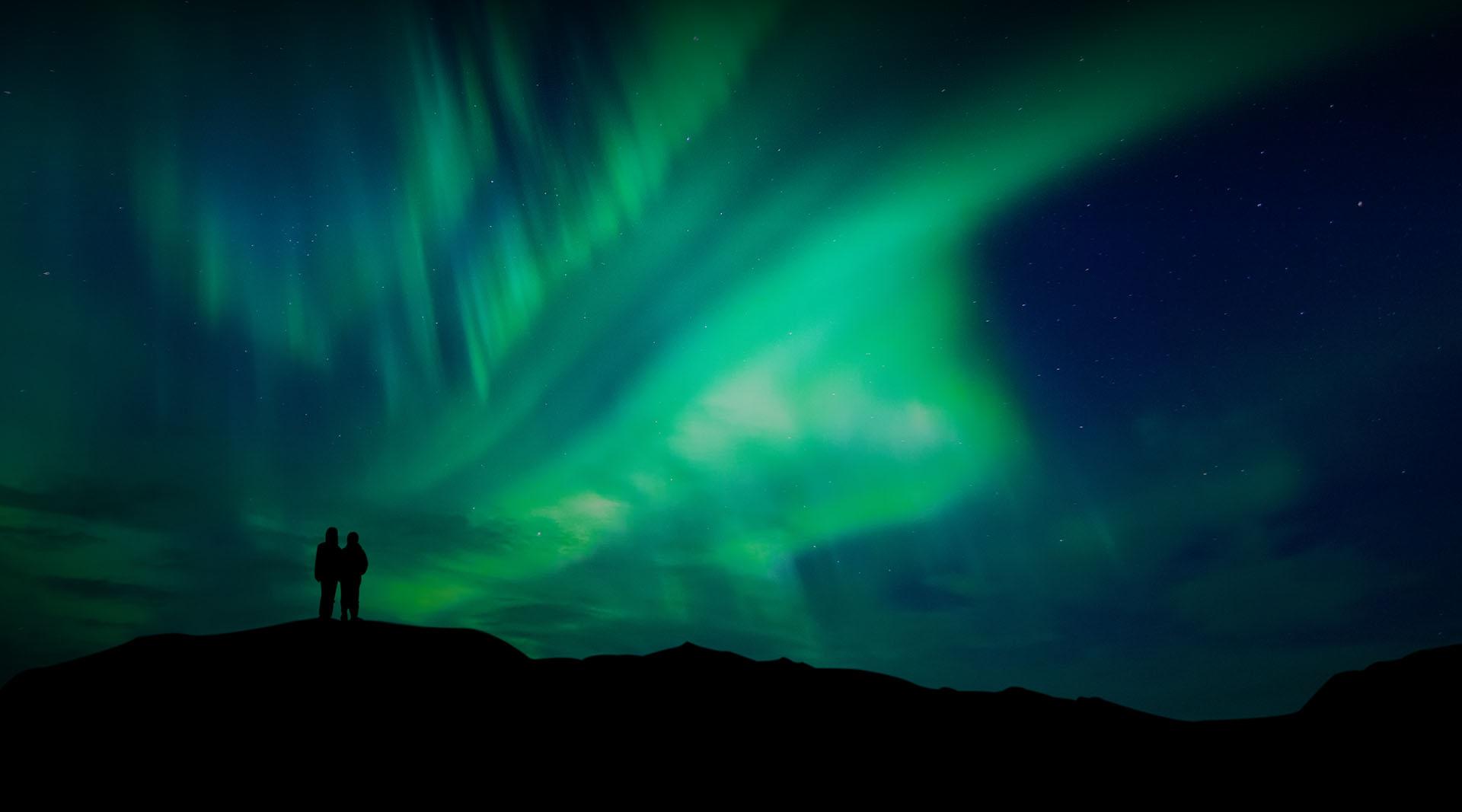 Silhouetted couple observing Aurora borealis.