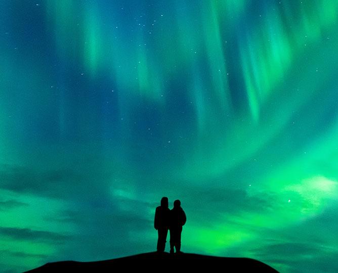 Silhouetted couple observing Aurora borealis.